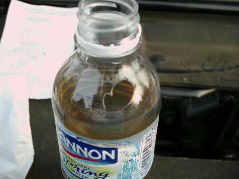 2002 Ford F-250 - Draining fuel filter into a water bottle, with a portion of a Ford engine in the background.