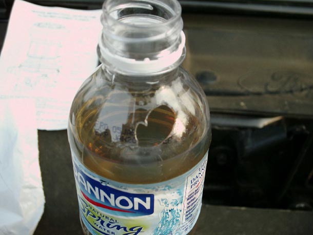 Water bottle holding amber diesel fuel drained from a filter housing, on a black engine cover