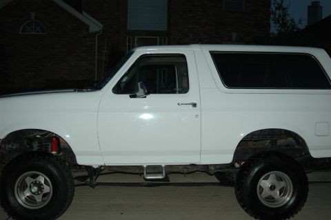 1992 Ford Bronco - The side profile of a white Ford Bronco is captured in this image, showing its lifted suspension and custom wheels.