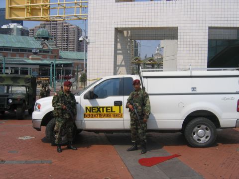 2000 Ford Crown Victoria - A white pickup truck with a camper shell, marked as a Nextel Emergency Response Vehicle, is parked next to two soldiers.
