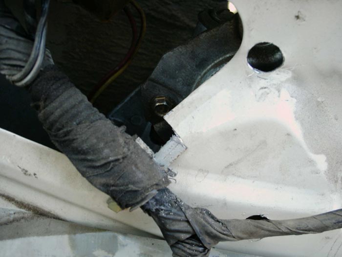 Notch cut in white metal panel near bolt, with cloth-taped bundle and dark bracket