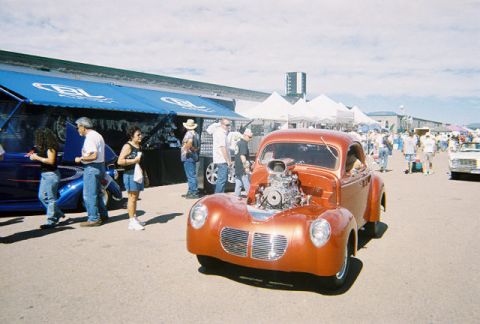 1972 Ford Ranchero - An orange hot rod with a large engine is parked at an outdoor event with people around.