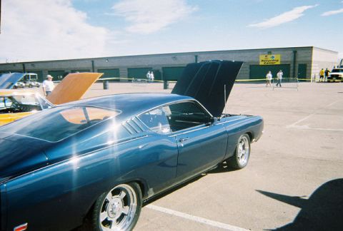 1972 Ford Ranchero - A blue coupe with its hood open is parked at an outdoor event, with other vehicles and a building in the background.