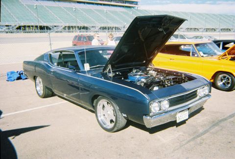 1972 Ford Ranchero - A blue coupe, likely from the early 1970s, is displayed with its hood open, revealing the engine bay, next to a yellow vehicle.