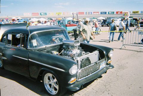 1972 Ford Ranchero - A heavily modified 1955 Chevrolet sedan is displayed at an outdoor car event with spectators in the background.