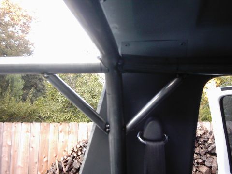 1978 Ford Bronco - Roll cage installation inside a vehicle, with exterior view of a fence and firewood.
