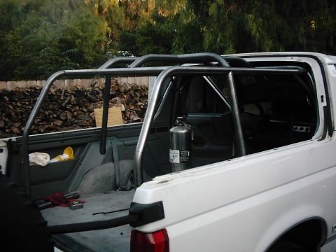1978 Ford Bronco - The interior of a white SUV is shown with a custom roll cage installed and a fire extinguisher mounted.