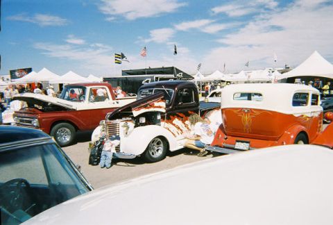 1972 Ford Ranchero - A custom hot rod pickup truck with a flame paint job is displayed at an outdoor event with other vehicles.