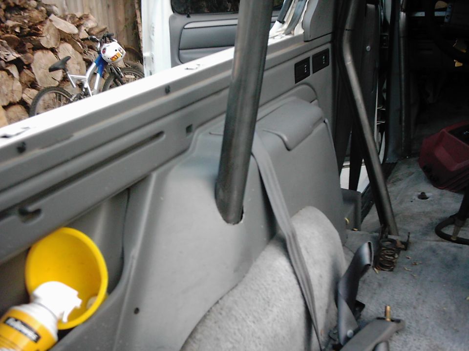 Interior of a vehicle with a roll cage, gray plastic trim, and a yellow funnel with a can. A bicycle is visible through the window