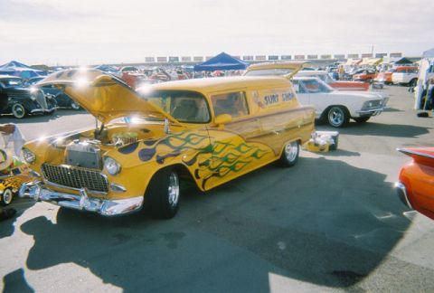1972 Ford Ranchero - A yellow panel van with flame graphics and "Surf Shop" lettering is displayed with its hood open at an outdoor event.