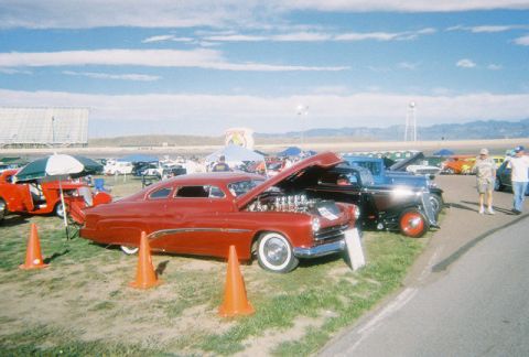 1972 Ford Ranchero - A custom red coupe from the 1950s is displayed with its hood open, revealing a V8 engine at an outdoor car show.