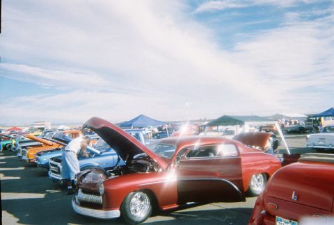 1972 Ford Ranchero - A line of cars with hoods up at an outdoor event under a blue sky with scattered clouds.