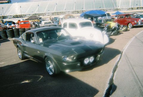 1972 Ford Ranchero - A dark gray 1967 Ford Mustang Fastback is parked at a car show with other vehicles in the background.