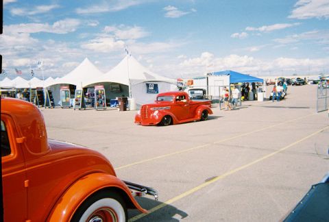 1972 Ford Ranchero - A bright red hot rod pickup truck is the main focus at an outdoor event with tents and other vehicles in the background.