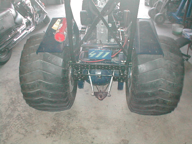 Rear of tube-frame buggy with wide paddle tires and '411' plate in a garage