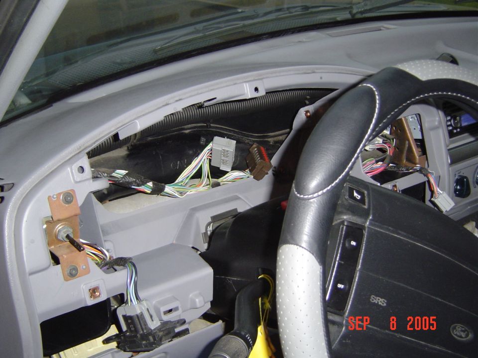 Gray dash disassembled showing wiring harnesses behind removed gauge cluster, black steering wheel at right