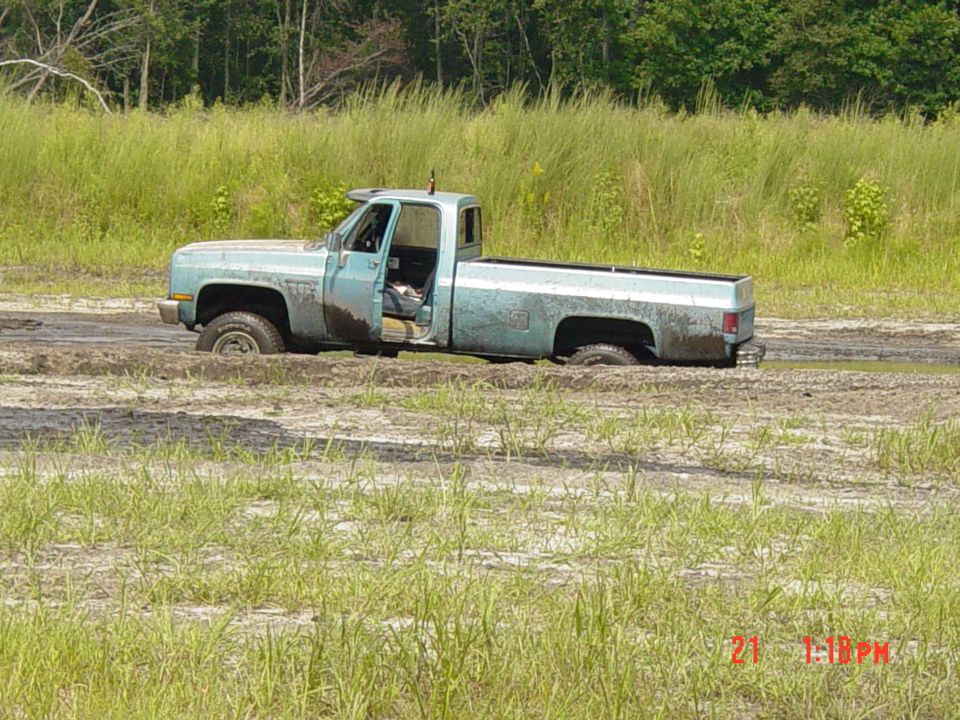 Light blue pickup truck stuck in mud, driver's door open
