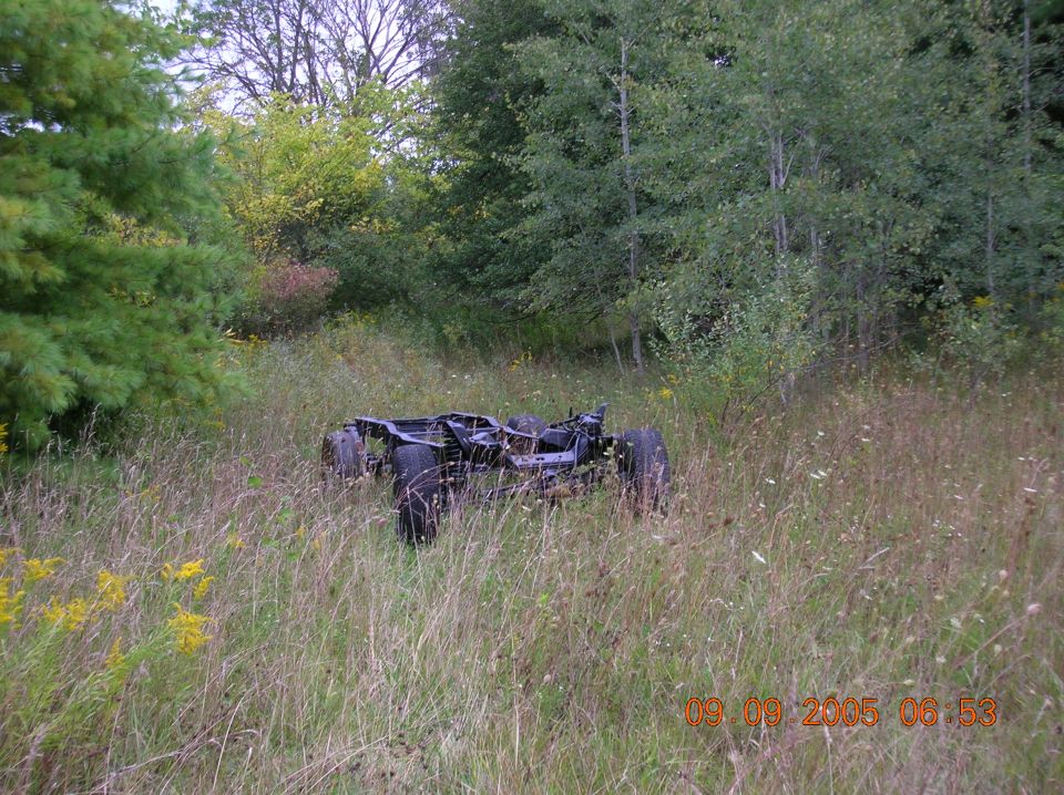 Vehicle frame and chassis with wheels sitting in tall grass and weeds