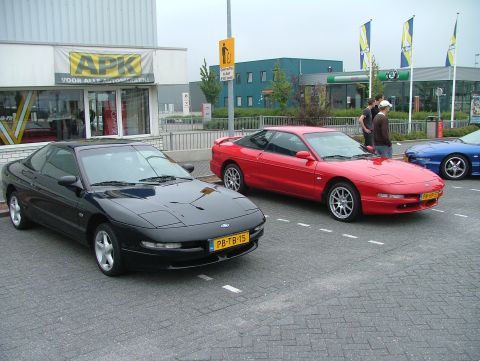 1994 Ford Probe - Two Ford Probes, a black and a red model, are parked side-by-side in a lot outside a business.