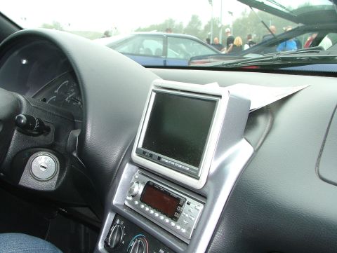 1994 Ford Probe - The dashboard of a car features an aftermarket stereo and a small screen, with another vehicle visible outside.