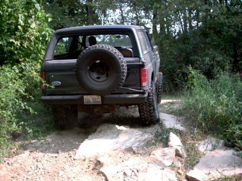 1986 Ford Bronco - This 1986 Ford Bronco navigates a rocky off-road path surrounded by trees and vegetation.