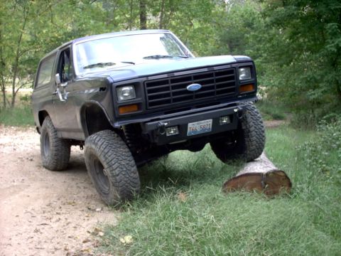 1986 Ford Bronco - This 1986 Ford Bronco is shown navigating an obstacle on a dirt path surrounded by trees.