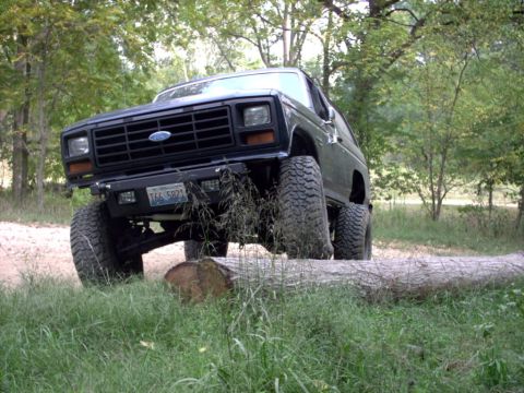 1986 Ford Bronco - This lifted Ford Bronco is navigating an obstacle on a wooded trail.
