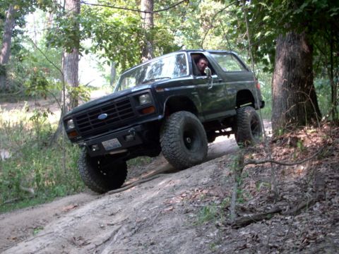 1986 Ford Bronco - A black 1980 Ford Bronco navigates a steep, wooded trail.