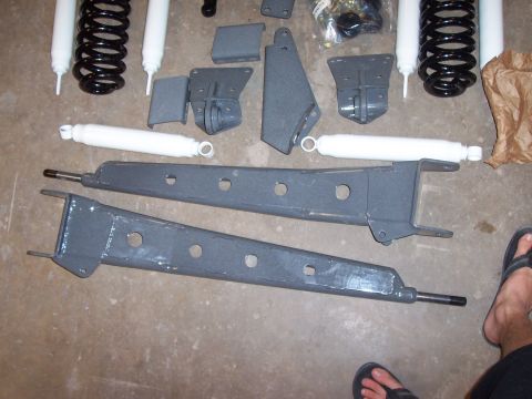 1996 Ford Bronco - Various gray lift kit components, including shocks and control arms, are laid out on a concrete surface.