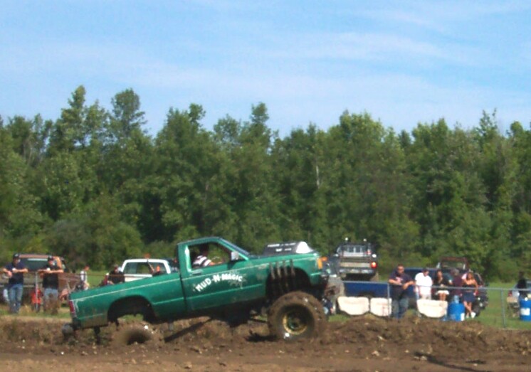 Green lifted pickup on tall tires climbing out of mud bog with rear wheels spinning