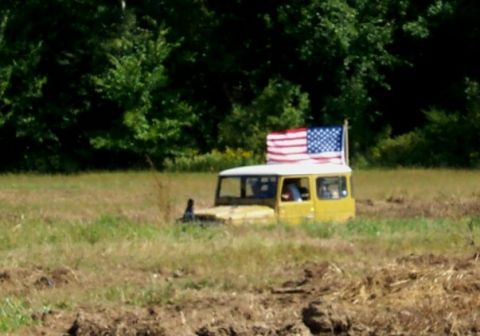1979 Ford F-150 - An American flag flies atop a yellow vehicle partially submerged in a muddy field.