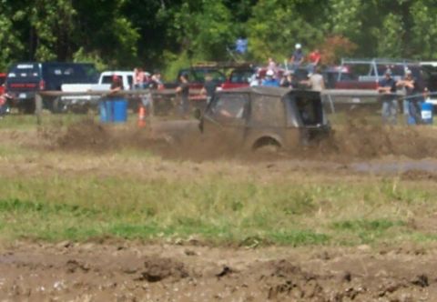 1979 Ford F-150 - An off-road vehicle navigates a muddy track during an event, with onlookers gathered nearby.