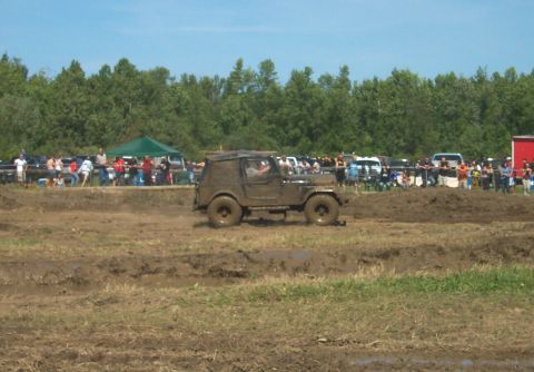 1979 Ford F-150 - An off-road vehicle navigates a muddy track during an event, with a crowd watching from the sidelines.