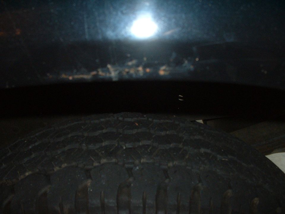 Close-up of a tire tread in dim lighting beneath a dark body panel