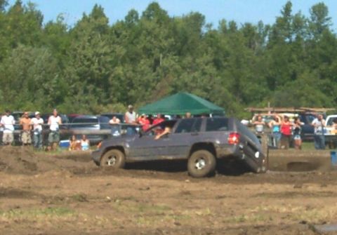 1979 Ford F-150 - A gray SUV navigates a muddy obstacle course, with one wheel significantly lifted off the ground.
