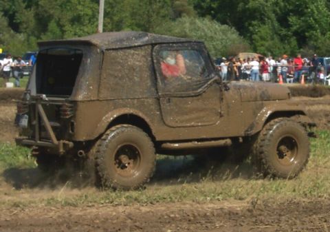 1979 Ford F-150 - A Jeep covered in mud navigates a muddy track, kicking up dirt as it goes.