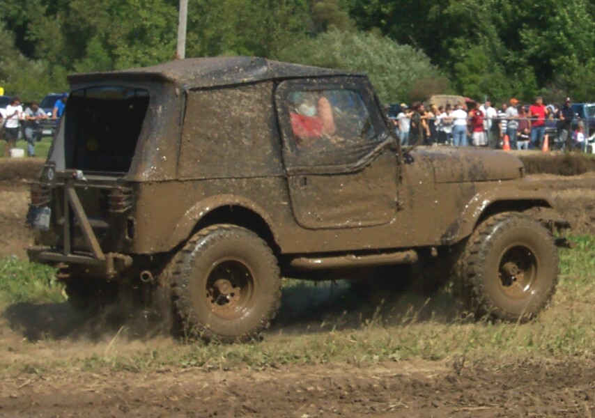 Muddy Jeep driving through a dirt track with spectators in the background
