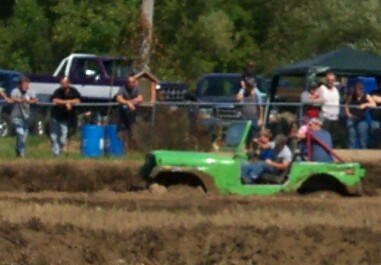 1979 Ford F-150 - A green Jeep navigates a muddy track with spectators observing the event.