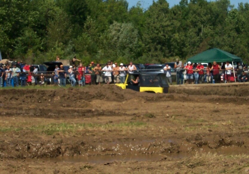 Yellow and black off-road vehicle with a driver, stuck in mud during an event