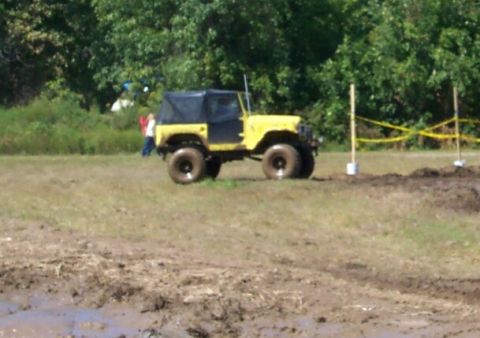 1979 Ford F-150 - A yellow jeep with a black soft top navigates a muddy off-road course.