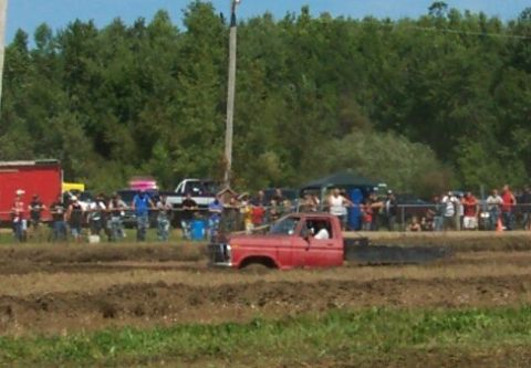1979 Ford F-150 - A red pickup truck is stuck in a mud pit during an event, with spectators gathered around.