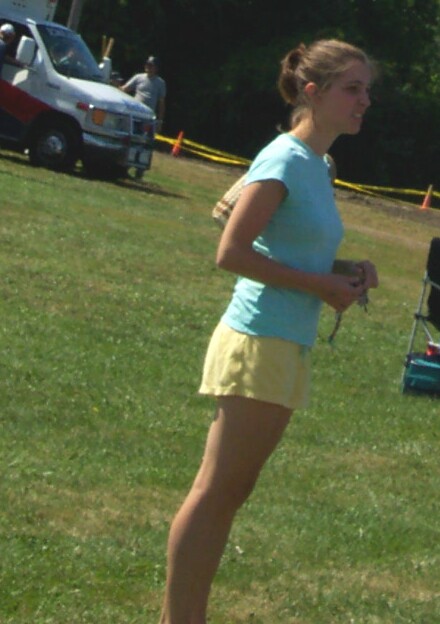 1979 Ford F-150 - A young woman in a light blue t-shirt and yellow shorts stands on a grassy field at an outdoor event, with a white van and yellow caution t…