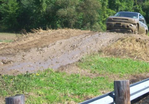 1979 Ford F-150 - A light-colored SUV is partially submerged in mud as it attempts to navigate a challenging off-road course.