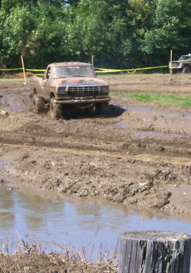 Muddy pickup truck driving through a mud pit. Another truck is visible in the background