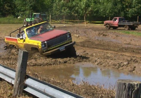 1979 Ford F-150 - A yellow and red pickup truck navigates a muddy obstacle course with another truck in the background.