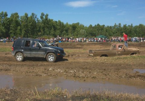 1979 Ford F-150 - A muddy 1979 Ford F-150 is stuck in a mud bog while a Jeep Liberty drives past, with spectators in the background.