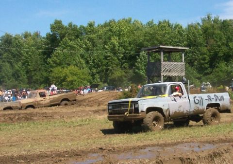 1979 Ford F-150 - Two pickup trucks are stuck in the mud at an outdoor event with spectators in the background.