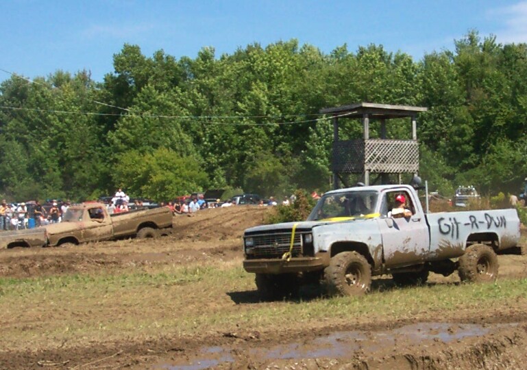 Light blue pickup truck with "Git-R-Dun" written on the side, stuck in mud