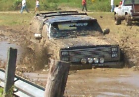 1979 Ford F-150 - Ford Bronco tackles a muddy obstacle course, with spectators watching.