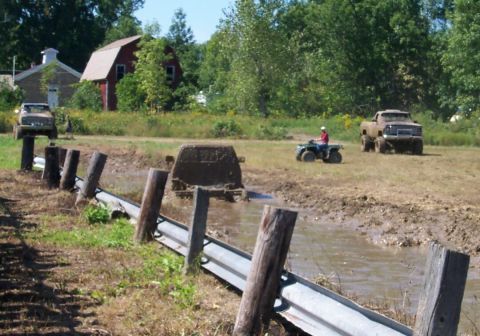 1979 Ford F-150 - Several vehicles are navigating a muddy obstacle course with farm buildings in the background.